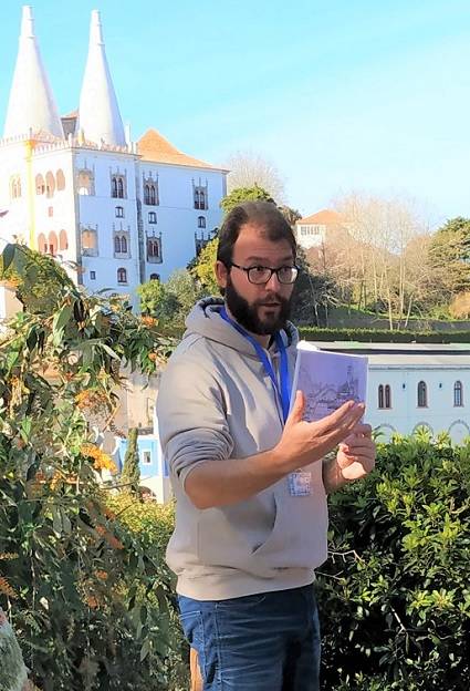 El guia Manu realizando el free tour de Sintra y explicando con el palacio nacional de Sintra a sus espaldas y rodeado de naturaleza exuberante.