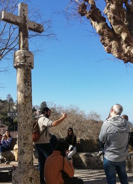 El guia Manu esta en mitad del Freetour de Sintra rodeado de viajeros que escuchan sus historias. Tras el un cruceiro que marca el final de la vila de Sintra.